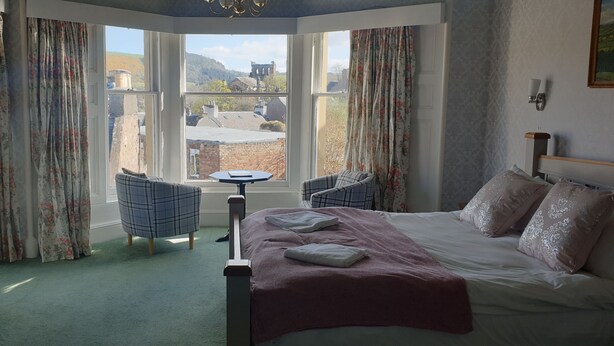 A bedroom with a bed, two chairs, a small table, and a TV. - George and Abbotsford Hotel (Melrose)