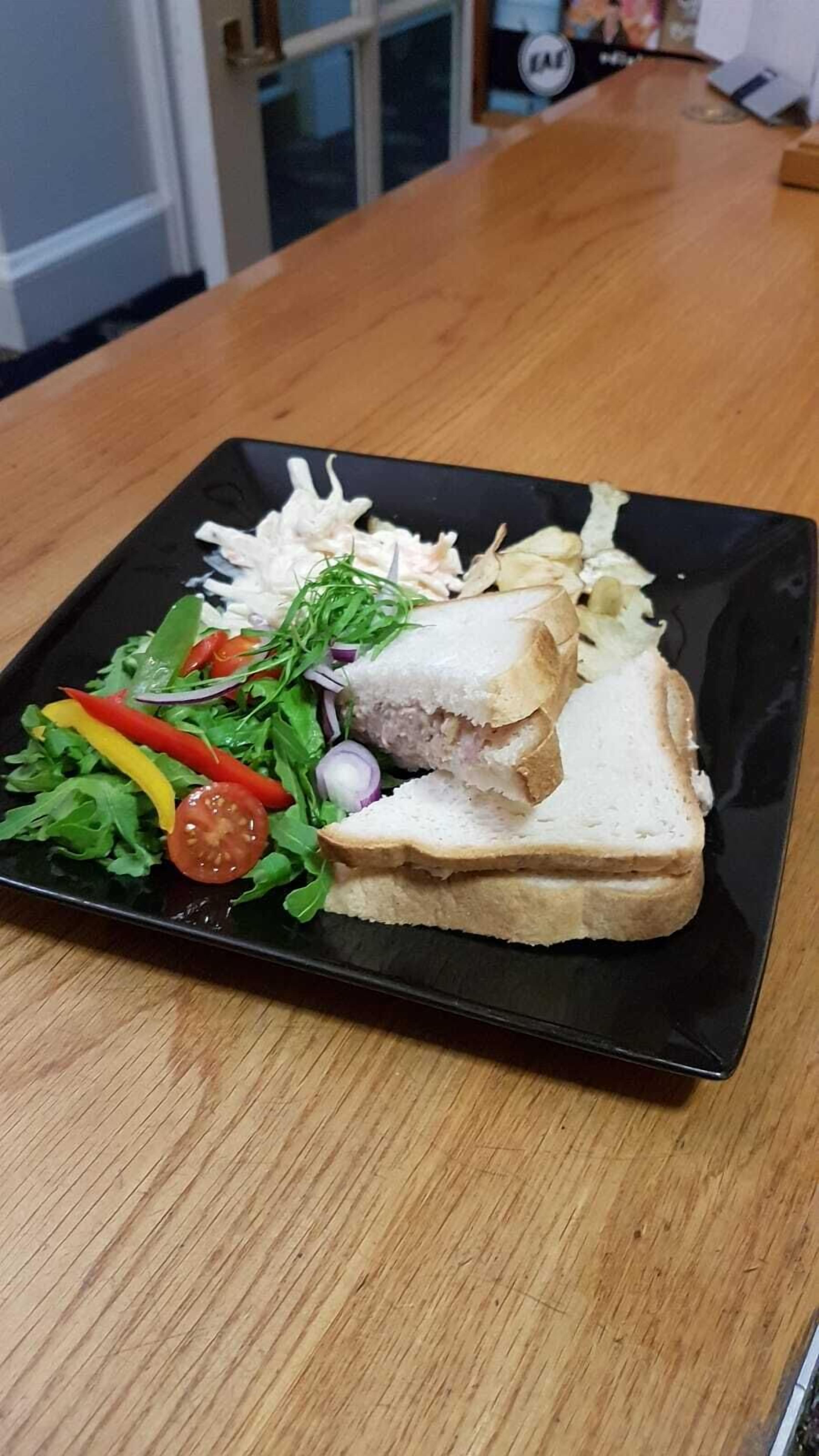 Un sándwich sobre un plato negro, acompañado de una ensalada.