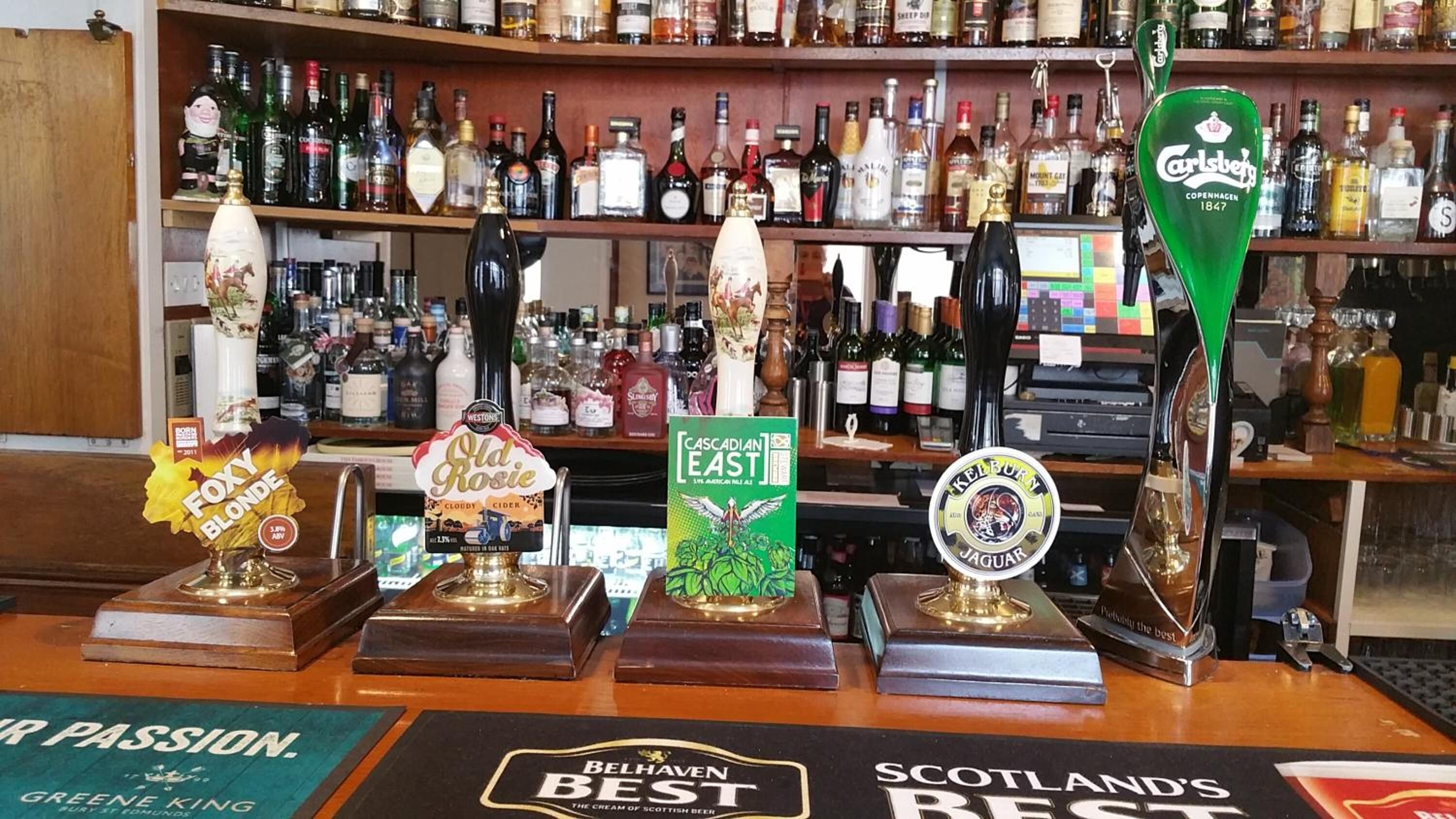 A bar with various beer taps and a shelf of liquor bottles.