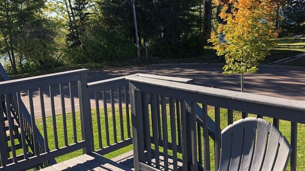 Eine Holzterrasse mit einem Stuhl, umgeben von Bäumen und einer Straße.