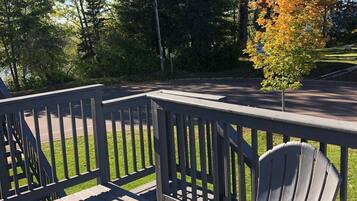 A wooden deck with a chair, surrounded by trees and a road.