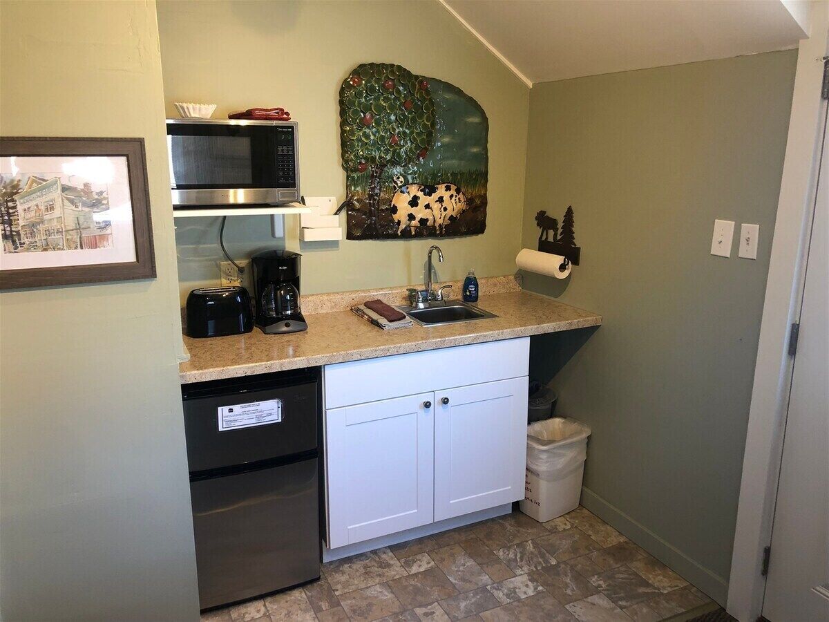 A compact kitchen with a microwave, toaster, sink, and a painting of a cow.