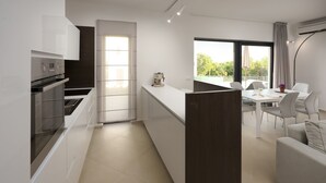A modern kitchen with a central island, a dining area with a table and chairs, and a large window with a view of greenery. - Villa Krnica (Marcana)