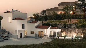 Et moderne hus med to etager, hvide facader, en stenvæg og en lille swimmingpool.
