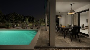 Et poolområde med spisebord og stole, omgivet af plantekasser og udsigt til nattehimlen.