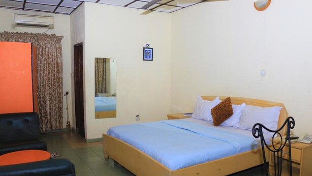A bedroom with a single bed, a nightstand, a chair, and a wardrobe. - The Noble Place (Calabar)