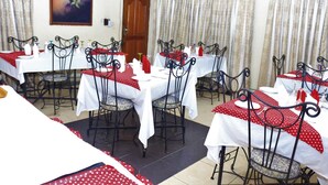 A dining area with multiple tables and chairs, each covered with white tablecloths and red polka dot table runners. - The Noble Place (Calabar)