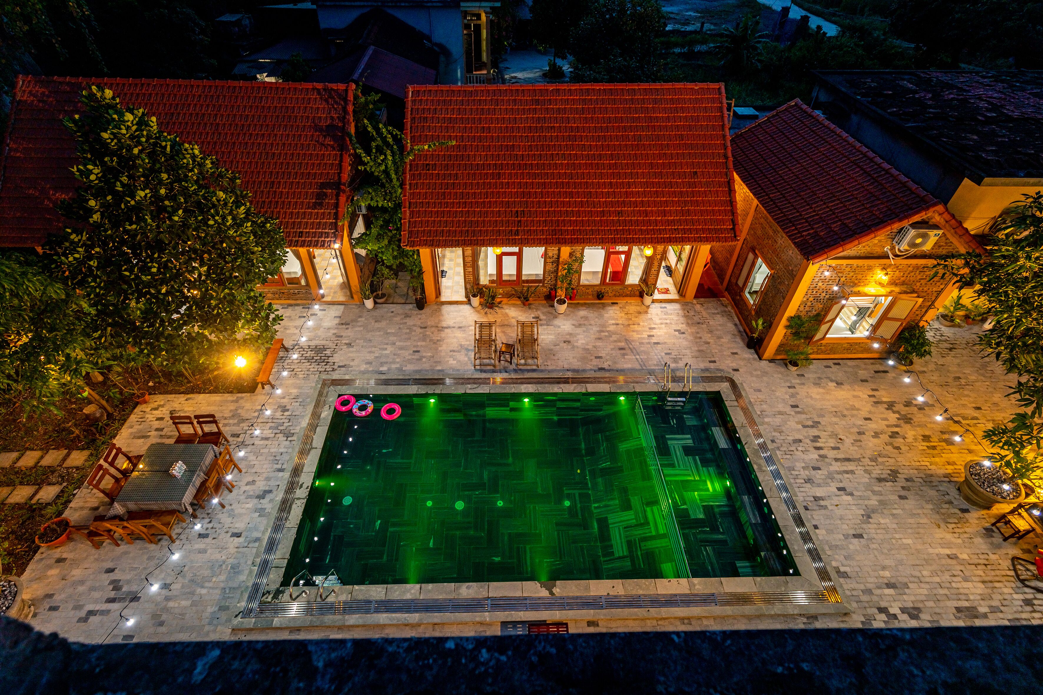 A swimming pool with a tiled deck, surrounded by outdoor furniture and potted plants.