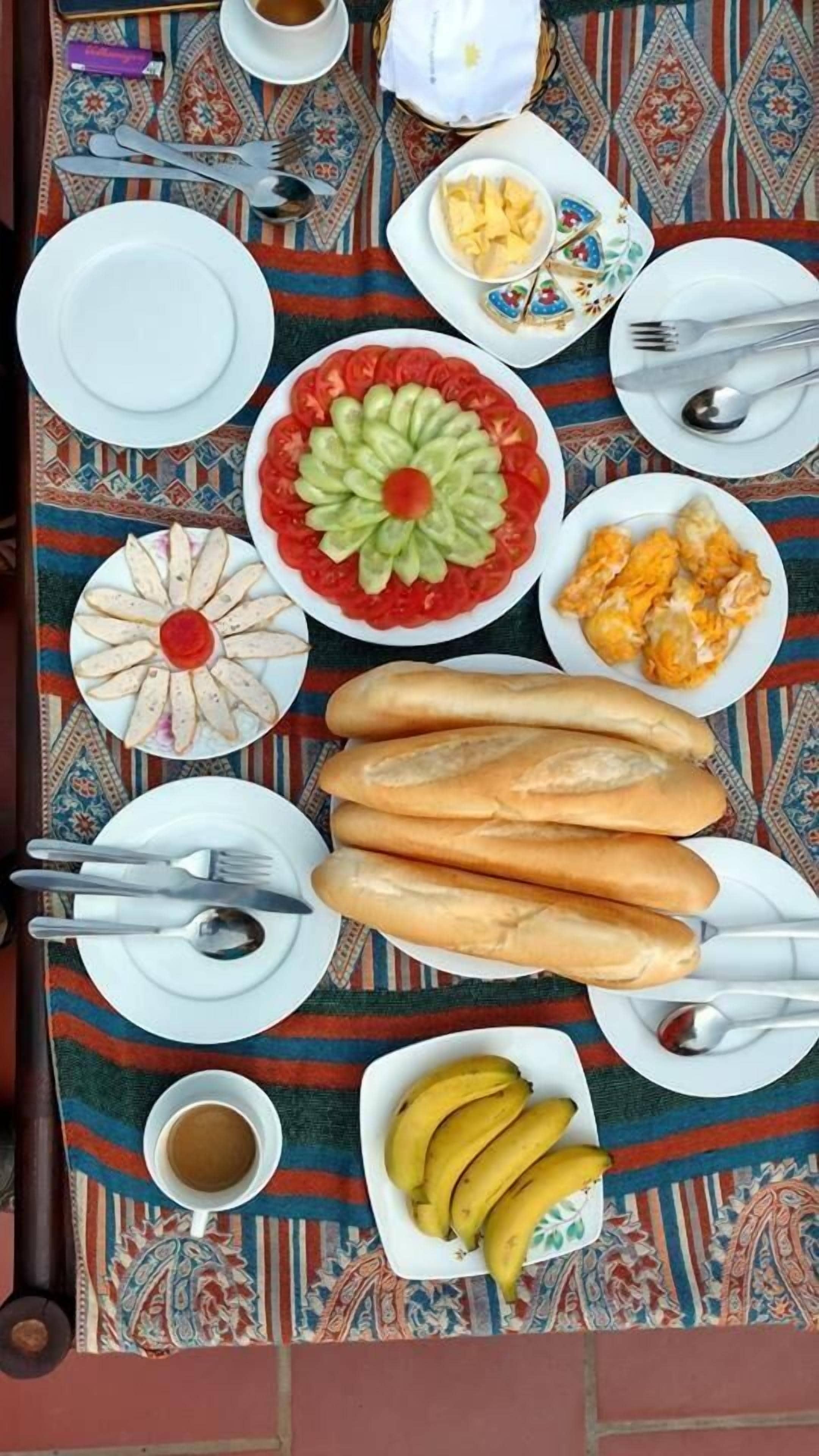 A table set with various dishes, including a flower-shaped salad, bread, and bananas, on a patterned tablecloth.