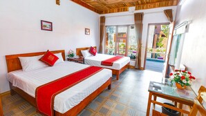 A hotel room with two beds, a wooden ceiling, a glass table with a vase of flowers, and a view of the outside.
