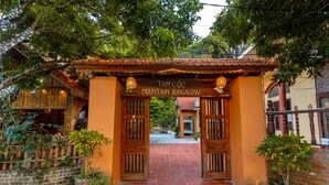 A wooden archway with a sign reading "TAM CÔC MOUNTAIN BUNGALOW" leading to a courtyard with potted plants and a tiled floor.