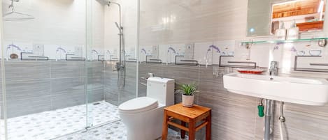 A modern bathroom with a glass-enclosed shower, a toilet, and a sink with a mirror above.