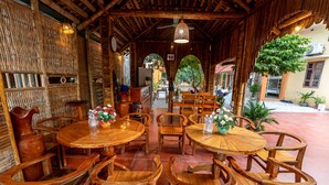 A rustic wooden dining area with round tables and chairs, a ceiling fan, and a view of the street outside.