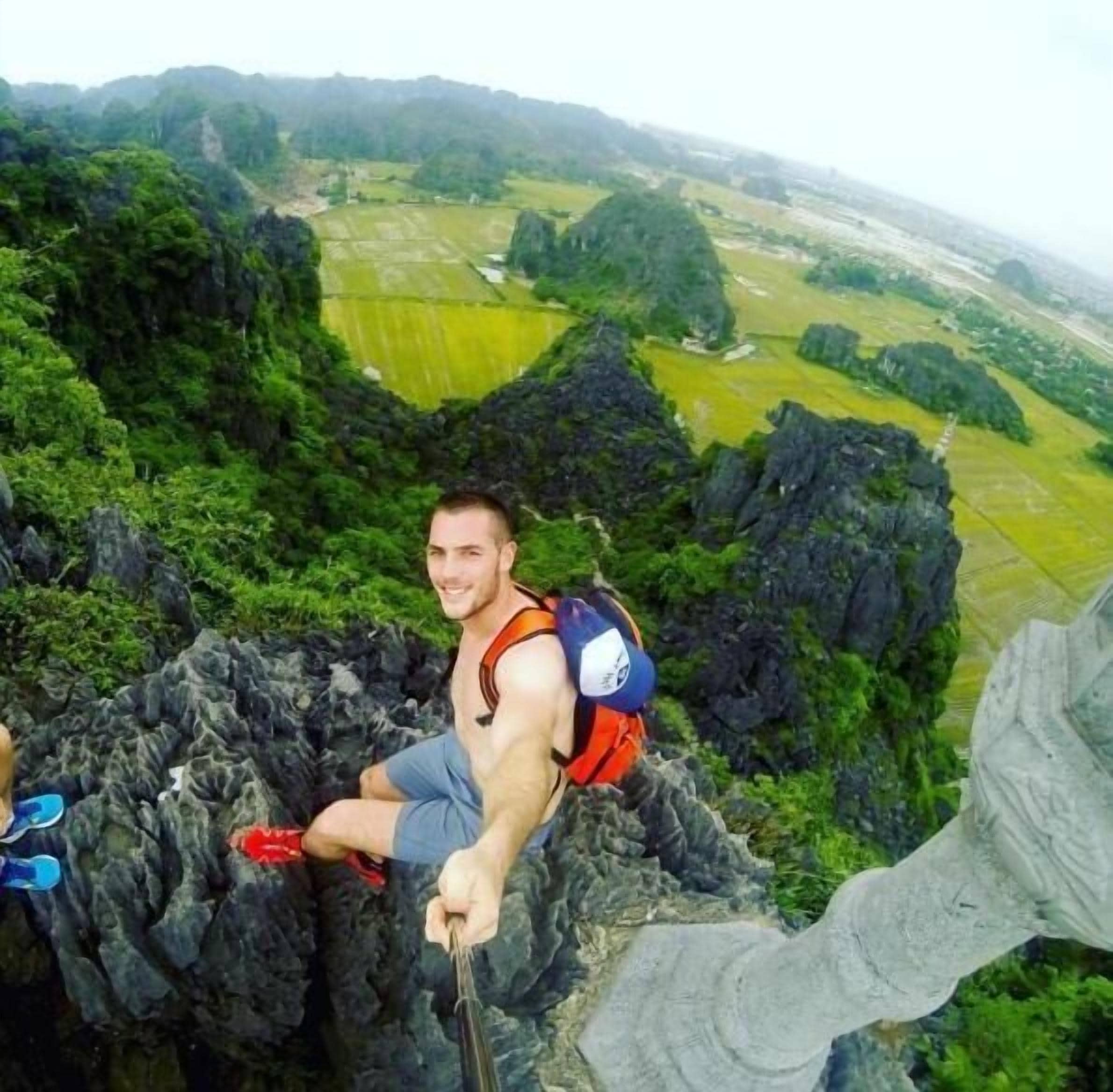 Una persona sentada sobre un afloramiento rocoso con una mochila, contemplando un valle con campos y montañas al fondo.