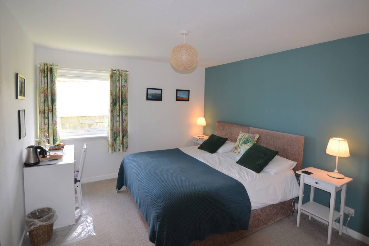 A bedroom with a bed, bedside tables, a desk, and a window with curtains.