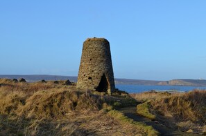 A stone tower with a single arched entrance, surrounded by grassy terrain and a body of water in the background. - Aurora B&B (Thurso)