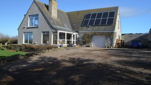 A two-story house with a sloped roof, a garage, and a solar panel installation on the roof. - Aurora B&B (Thurso)