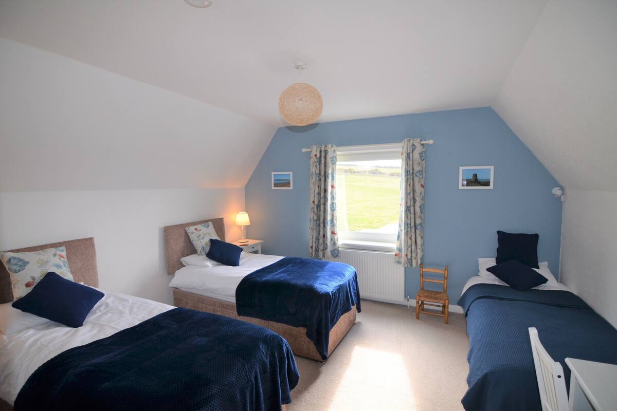 A bedroom with two beds, a window with curtains, a chair, and a small table.