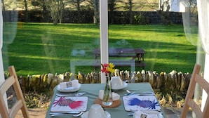 A dining table set for two with a view of a grassy garden through large windows. - Aurora B&B (Thurso)