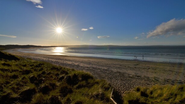 A beach with the sun setting over the horizon, grassy dunes, and a calm sea. - Aurora B&B (Thurso)