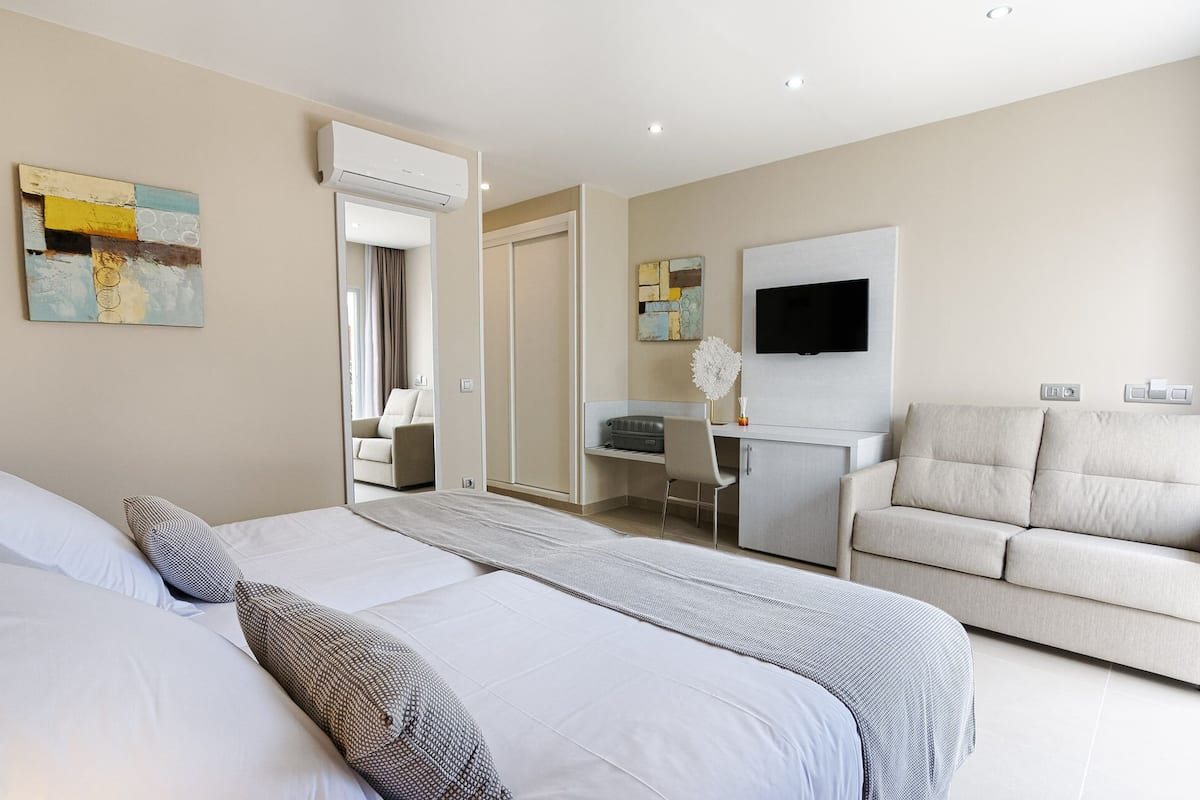 Ein Hotelzimmer mit Bett, Schreibtisch, Stuhl, Sofa, Fernseher und Bildern an der Wand.