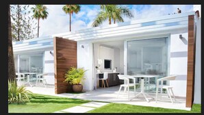 A modern, two-story house with a patio area featuring outdoor seating and a large window overlooking the garden.
