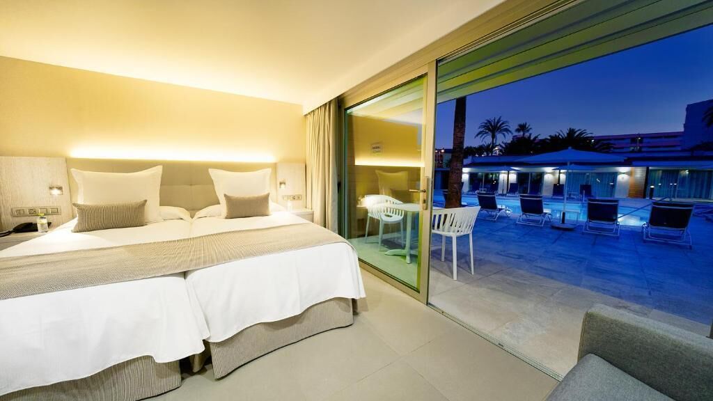 A hotel room with a bed, bedside tables, and a view of an outdoor pool area.