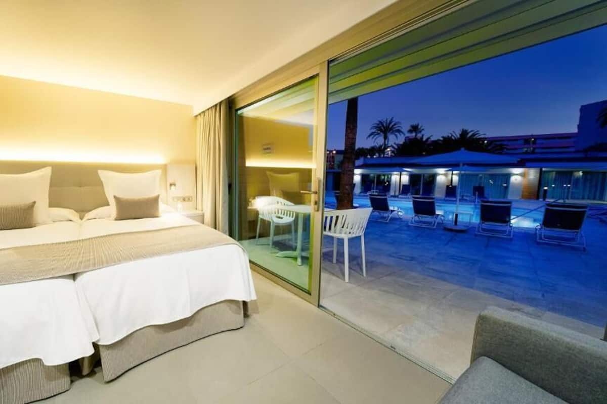 Ein Hotelzimmer mit einem Bett, Nachttischen und Blick auf einen Außenpool.