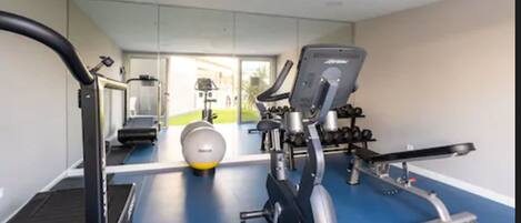 Un gimnasio con equipo de ejercicio, un espejo y vistas al exterior.