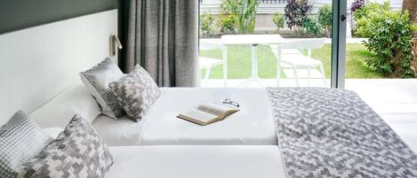 A modern bedroom with a white bed, patterned pillows, a book, and a pair of glasses.