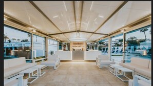 A modern hotel lobby with a reception desk, seating area, and large windows offering views of a pool and outdoor area.