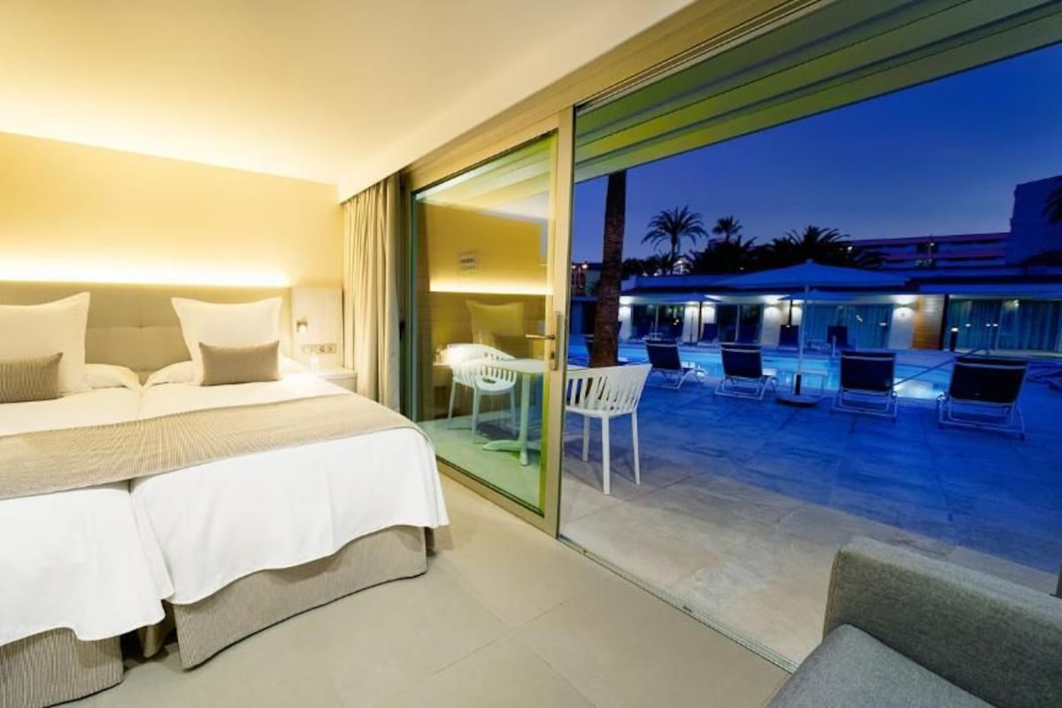 A hotel room with a bed, bedside tables, and a view of an outdoor pool area.