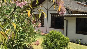 A house with a gabled roof and a garden with flowering plants and shrubs. - The Bridge To Ecuador (Pomasqui)