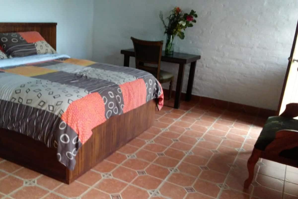 A bedroom with a bed, a chair, a small table, and a vase with flowers.