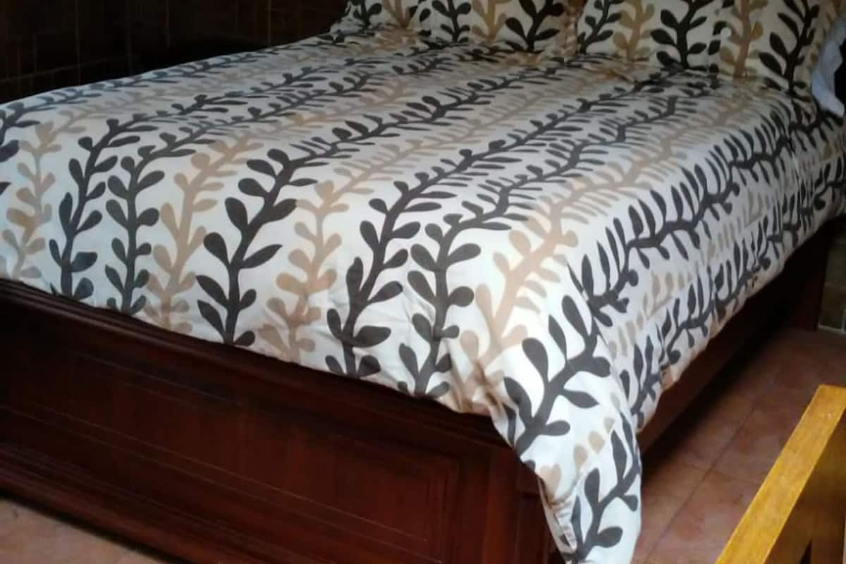 A bed with a patterned bedspread and matching pillows, a wooden headboard, and a tiled floor.