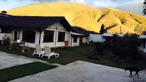 A house with a sloped roof, a front porch with chairs, and a mountain in the background. - The Bridge To Ecuador (Pomasqui)