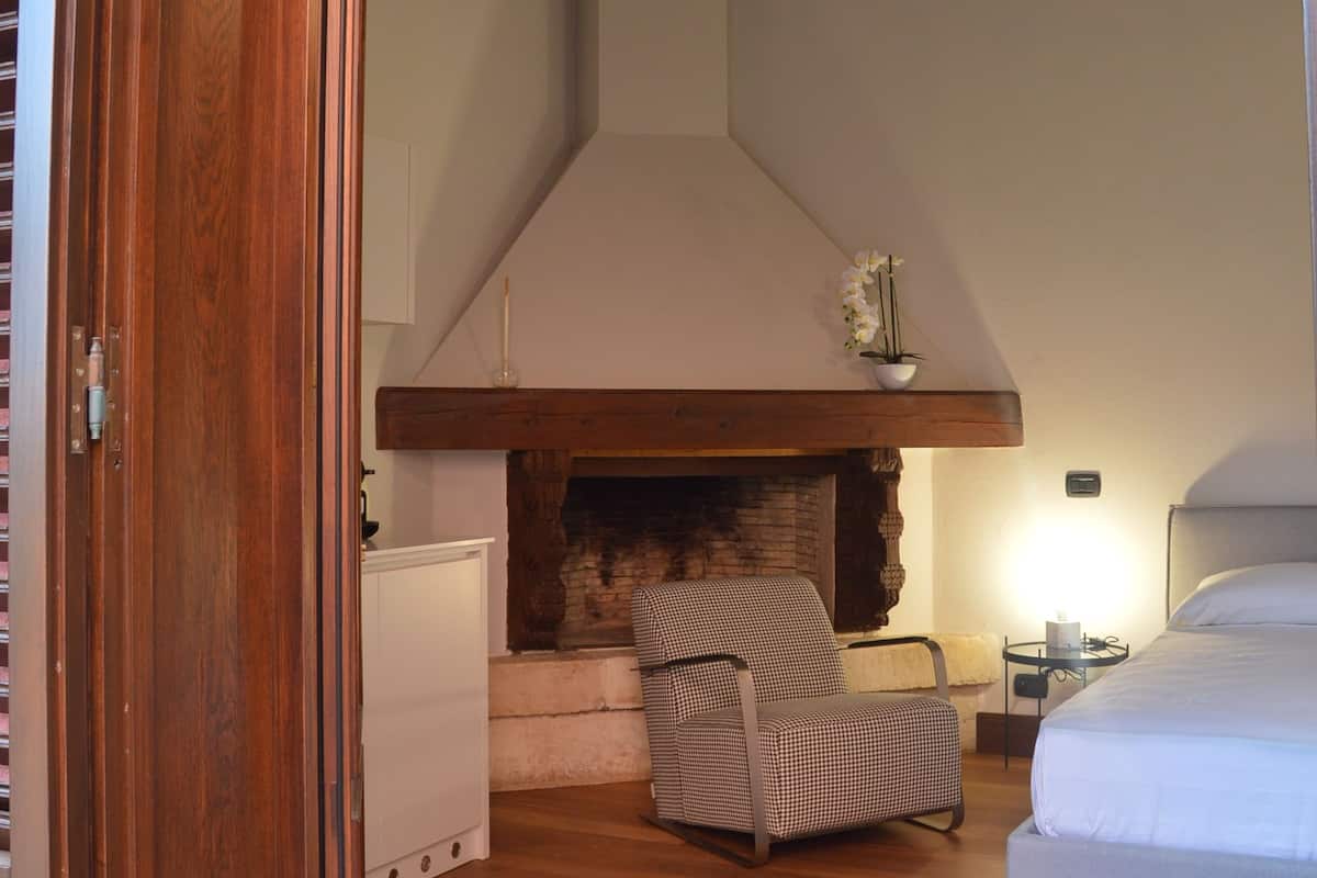 A bedroom with a wooden ceiling, a fireplace, a bed, and a chair.