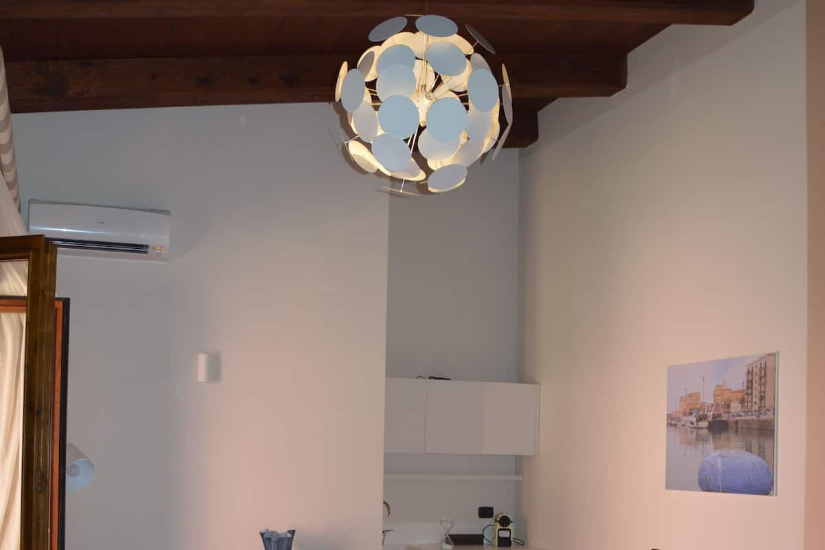A bedroom with a bed, a desk, a chair, and a hanging light fixture.