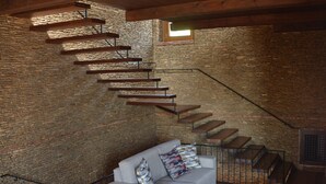 A modern interior with a staircase against a stone wall, a grey sofa with cushions, and a small table with items. - CasaRealia (Agrigento)