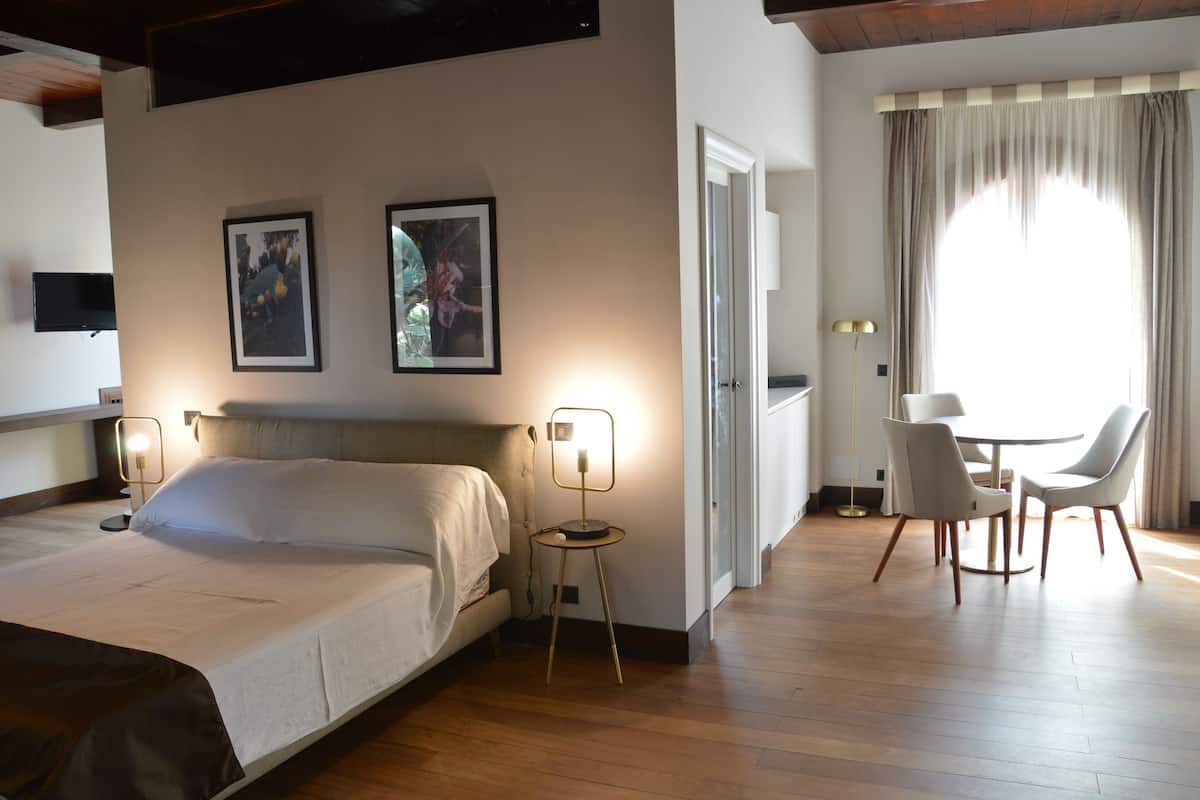 A hotel room with a bed, bedside lamps, a dining table with chairs, and two framed pictures on the wall.
