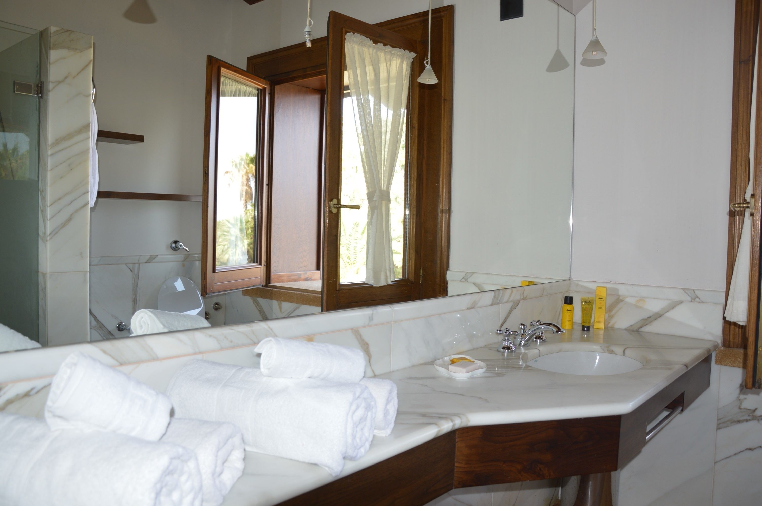 A bathroom with a large mirror, a sink, and a shower. There are towels on the counter and a window with curtains.