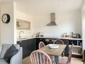 A compact kitchen with a central island, a built-in oven, and a microwave. There is a dining area with a wooden table and pink chairs.