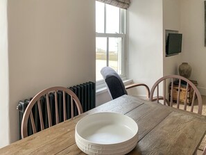 Ein Essbereich mit einem Holztisch, zwei Stühlen, einer weißen Schüssel, einem Heizkörper und einem Fenster mit Blick nach draußen.