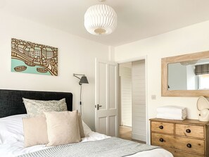 Ein Schlafzimmer mit einem Bett, einer Nachttischlampe, einem Schminktisch, einem Spiegel und einem Stadtbild an der Wand.
