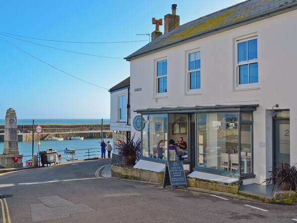 Ein Küstengebäude mit Café, Blick auf das Meer und einem Denkmal.
