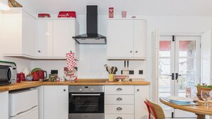 Une cuisine avec des meubles blancs, un four Bosch, une chaise rouge et une table en bois.