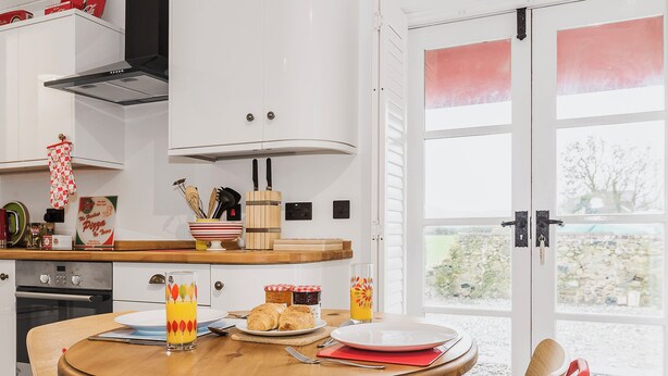 Une cuisine avec une table à manger, des chaises et une vue sur l’extérieur, visible à travers une porte vitrée.