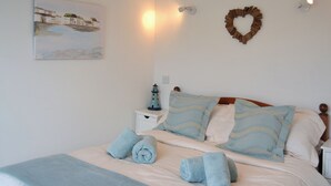 Cama bem arrumada com toalhas azuis, uma decoração de farol e uma pintura costeira na parede.