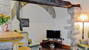 Uma sala de estar acolhedora com paredes de pedra, uma mesa de madeira com cadeiras, uma televisão e um abajur.
