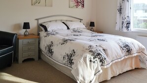 A bedroom with a bed, two bedside tables with lamps, a chair, and two floral paintings on the wall. - 4 bedroom accommodation in Keswick (Keswick)